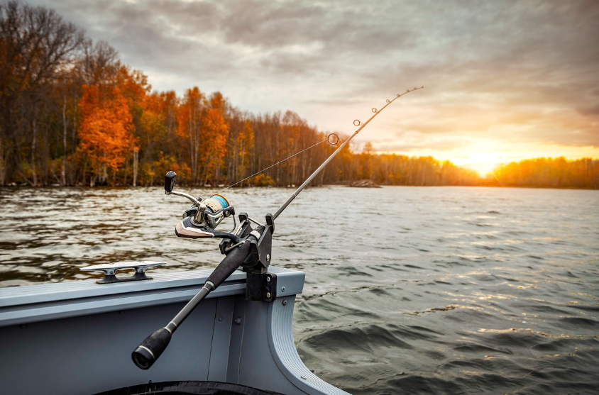 Fishing rod and reel mounted on a boat overlooking a freshwater lake at sunset